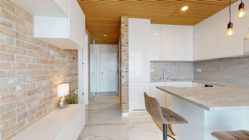 Brick wall in the kitchen of a two-room apartment with white furniture and marble floor.