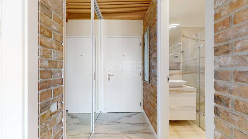 Hallway and bathroom in a 2-room apartment with a mirrored wardrobe and brick walls.