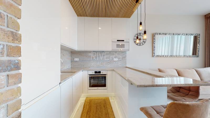 A kitchen in a 2-room apartment with white cabinets, brick detail, and natural stone.