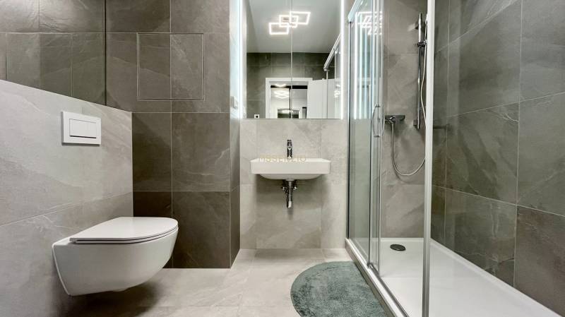 Bathroom in a 2-room apartment with a toilet, shower, and sink with tiles.