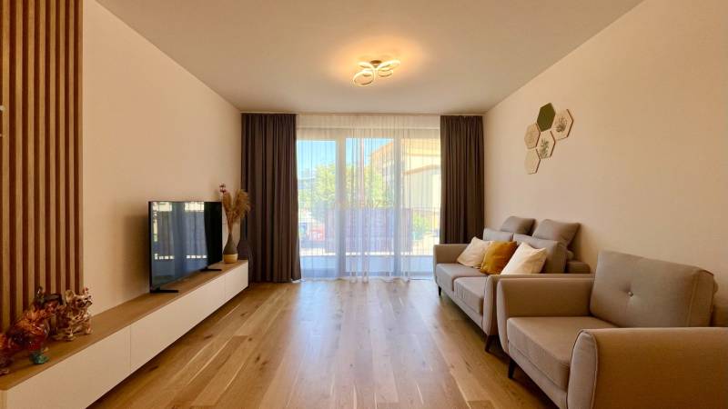 2-bedroom apartment with a sofa, television, wooden floor, and a shining chandelier.