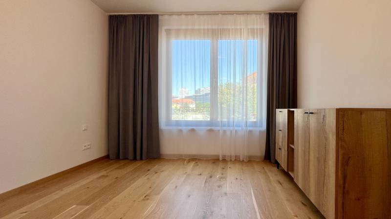 A spacious room with wooden flooring, curtains, and a dresser in a 2-room apartment.