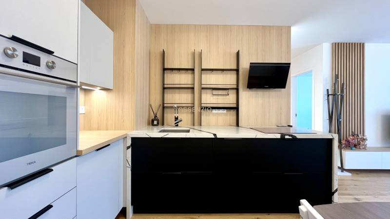 A kitchen in a 2-room apartment with white and black cabinets, a built-in oven, and wooden elements.