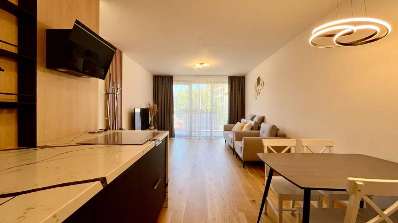 Living room in a two-room apartment with a kitchenette, wooden floor, and large window.