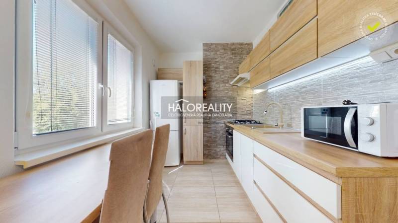 A kitchen in a 3-room apartment with built-in appliances, wooden cabinets, and a dining table.