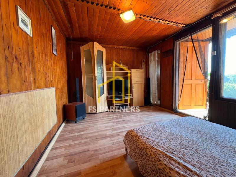 Wooden interior with a bed and a wardrobe, marked with the real estate agency's logo.