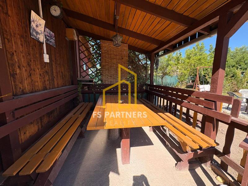 A wooden gazebo with a table and benches in the garden of Komárno, ideal for relaxation.