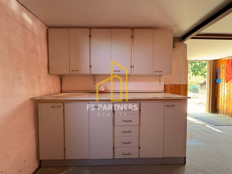 Simple kitchen unit in the interior, with cabinets and a sink, doors lead to the garden.