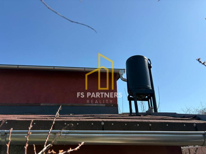 A roof with a water tank and details of gutters in the garden under the blue sky.