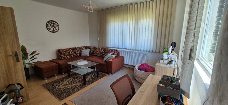 Living room with a brown sofa, glass table, and vertical blinds in a family house.
