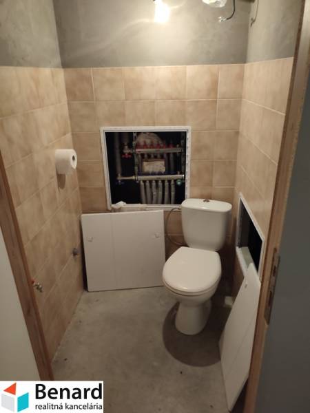 A bathroom in a family house with a toilet and exposed plumbing behind the tiles.