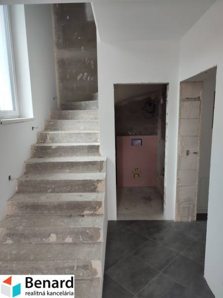 A staircase and an unfinished bathroom in a family house with gray tiles and white walls.