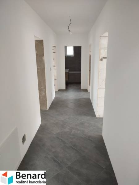 A hallway in a family house with white walls and gray tiles, without doors.