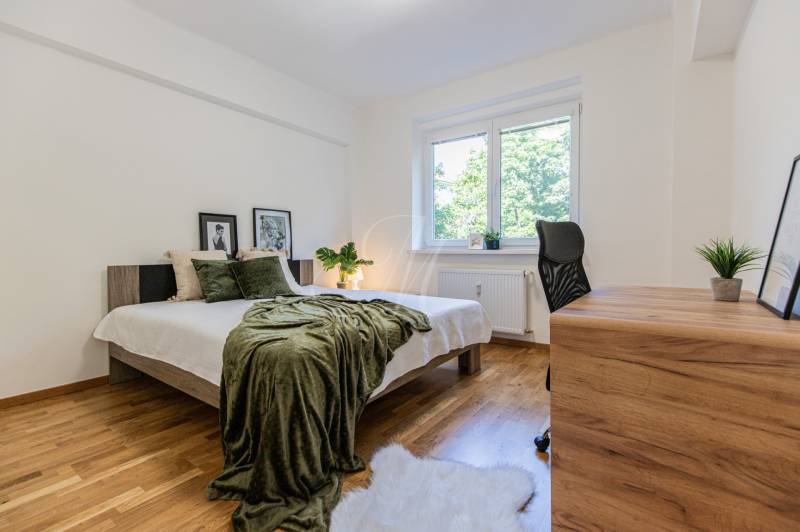 Bedroom in a 3-room apartment with a bed, wooden floor, and a desk.