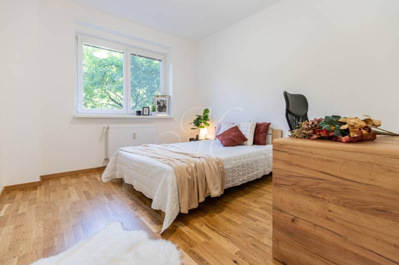 A bedroom in a 3-room apartment with wooden flooring and a view of greenery.