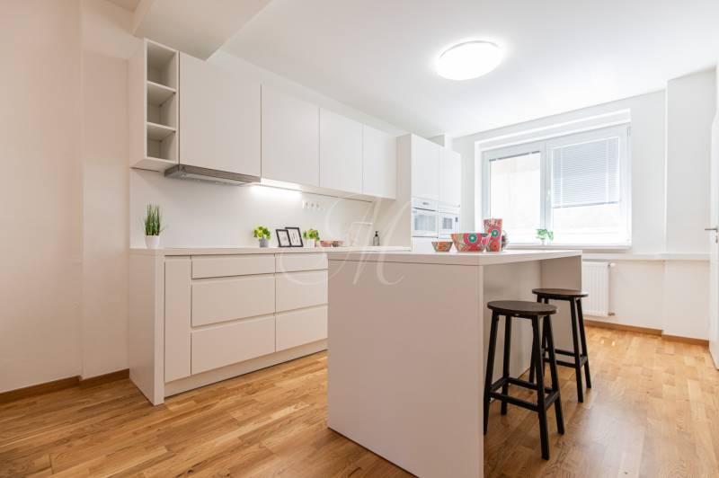 A kitchen in a 3-room apartment with wooden flooring, white cabinets, and a central island.