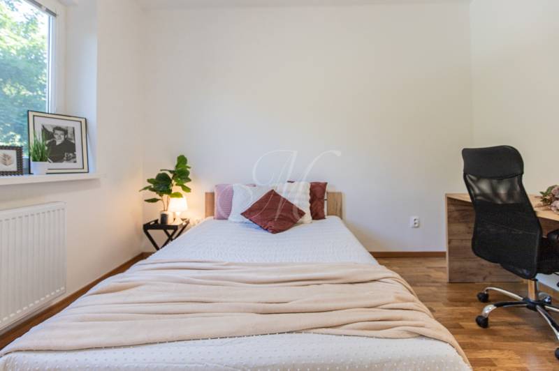 Bedroom in a 3-room apartment with a simple bed, a desk, and a plant.