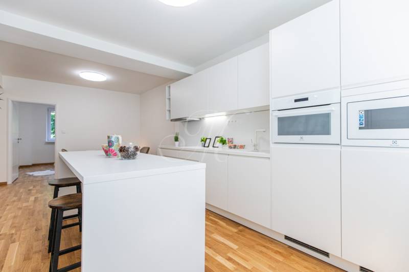 A kitchen in a 3-room apartment with white furniture and bar stools on a wooden floor.