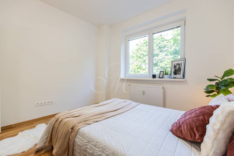 Bright bedroom in a 3-room apartment with a bed, blanket, and a window overlooking greenery.