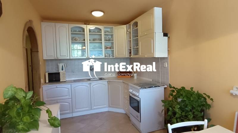 A kitchen in a 3-room apartment with a white kitchen unit, equipment, and greenery.