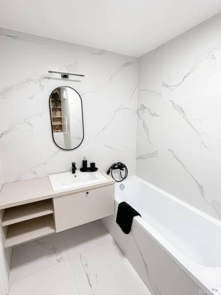 Bathroom in a 2-room apartment with a mirror and a bathtub, white marble tiles.