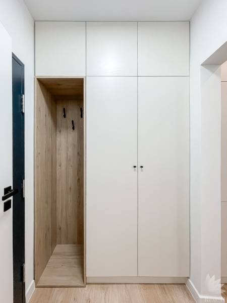 White built-in wardrobe with wooden detail and hooks in a 2-room apartment.
