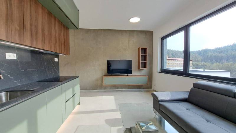 A kitchen unit with a TV and a couch in a 2-room apartment with a large window.