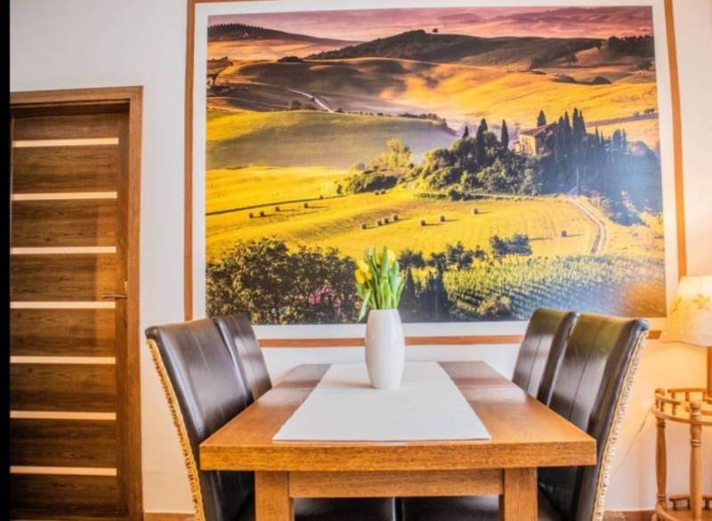 Dining table with a vase of tulips, large landscape photograph on the wall.