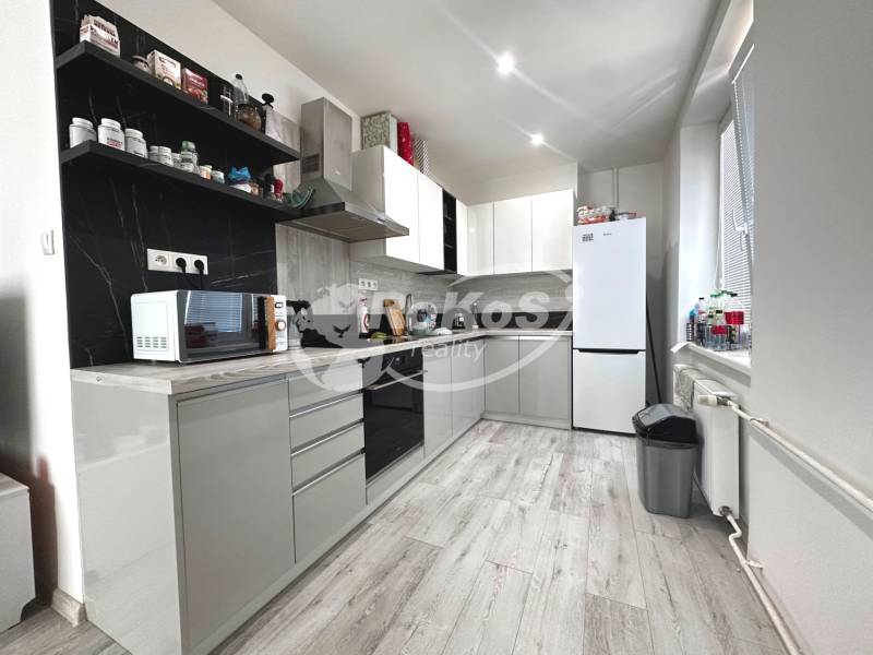 A kitchen in a 2-room apartment with white furniture, appliances, and black tiles.