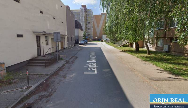 L. Novomeský Street in Pezinok with garages, residential buildings, and greenery.
