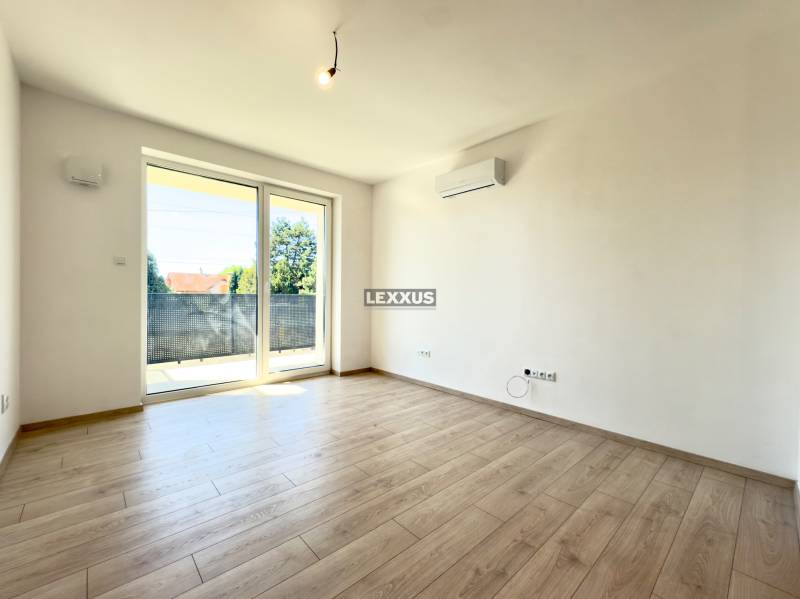 Living room with wooden flooring, balcony doors, and air conditioning in a 2-room apartment.