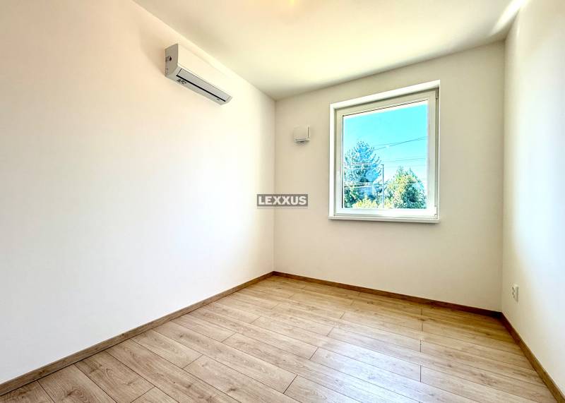 A bright room with wooden flooring, a window, and air conditioning in a 2-room apartment.