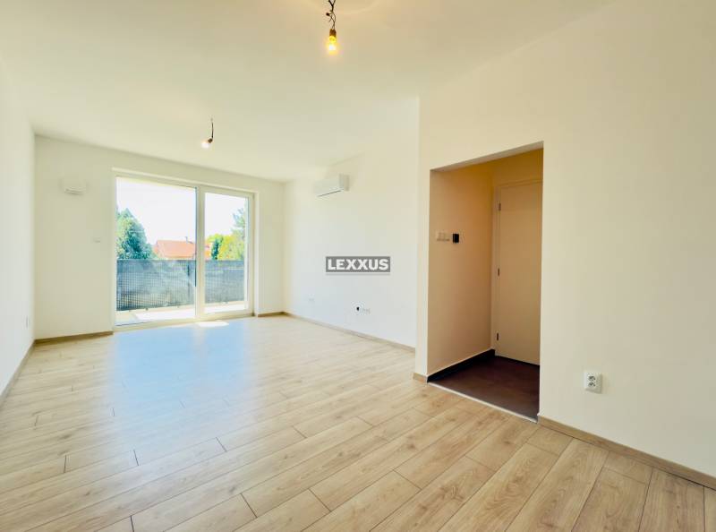 A bright living room with wooden flooring and balcony doors in a two-room apartment.
