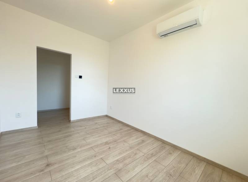 An empty room in a 2-room apartment with white walls and laminate flooring.