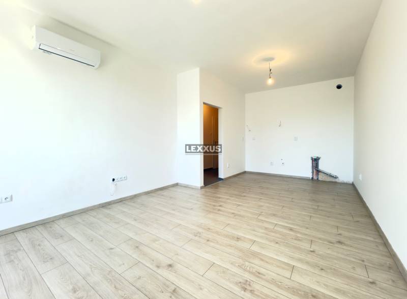 A room in a two-room apartment with air conditioning and wooden flooring, bright walls.