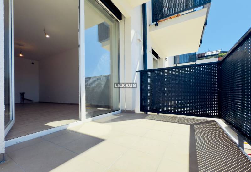 A balcony of a 2-room apartment with sliding doors and a view of the surrounding architecture.
