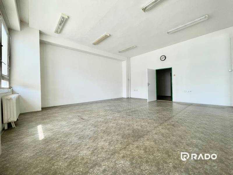 A spacious office with large windows, white walls, and ceiling lights.