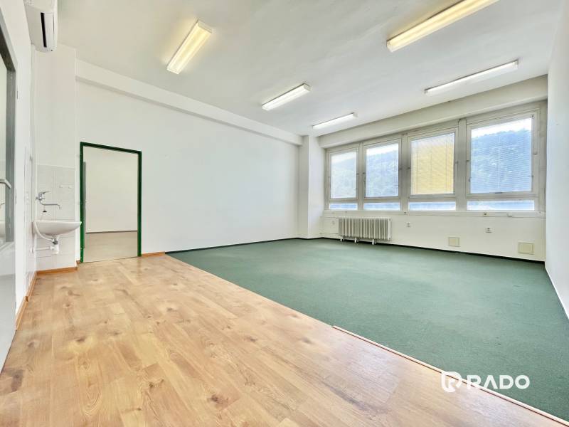 A bright office with windows, a sink, and mixed flooring.