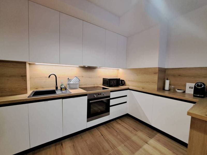 A kitchen unit in a 2-room apartment with white cabinets and a wooden countertop.