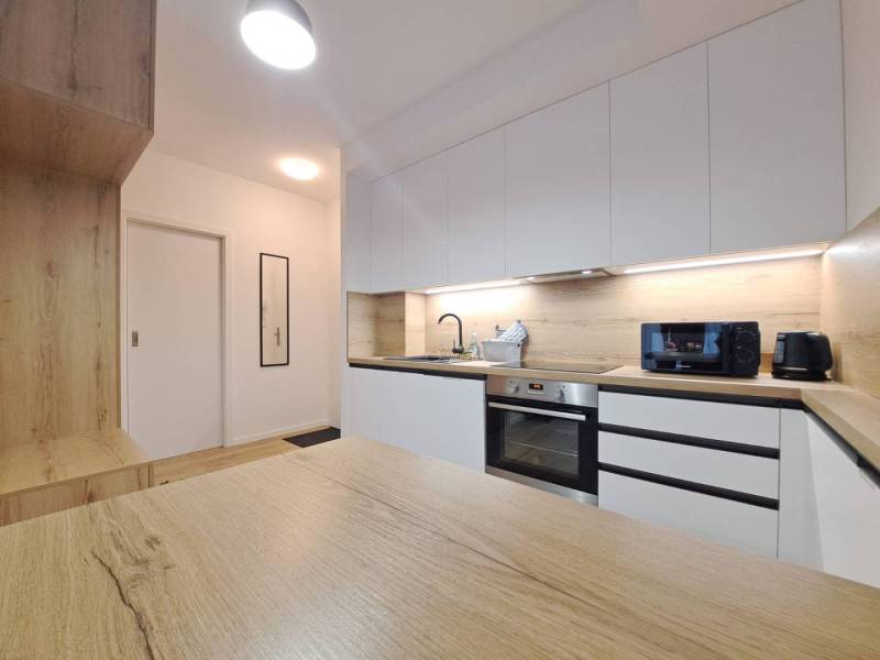 A kitchen in a 2-room apartment with a wooden countertop and white cabinets.