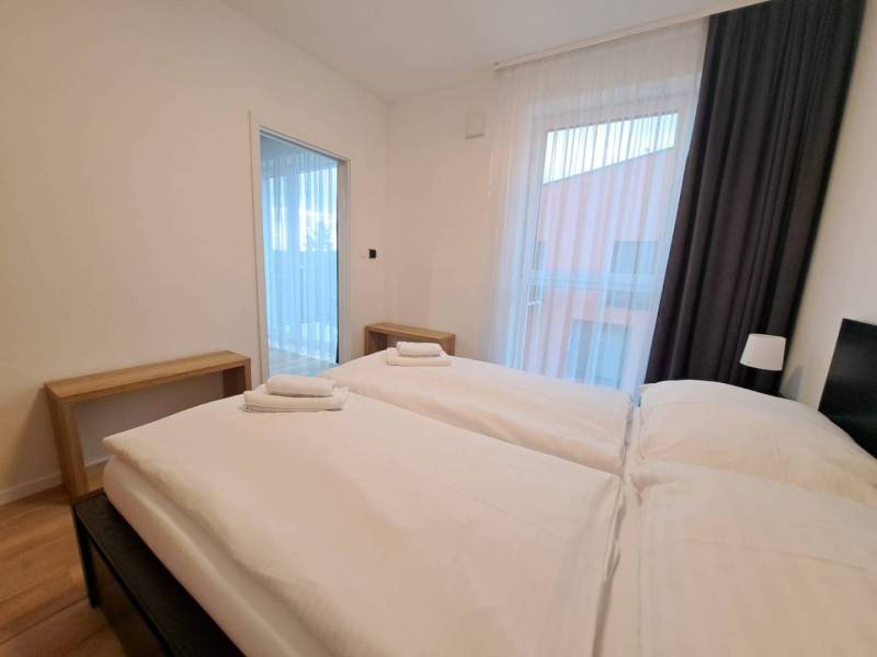 A bedroom in a two-room apartment with two beds, wooden tables, and curtains.