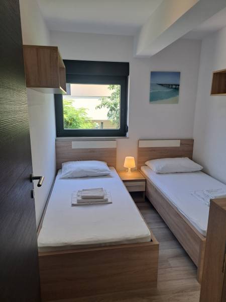 A room in a 3-bedroom apartment with two beds, a nightstand, and a window with a view.