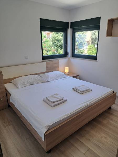 A bedroom in a three-room apartment with a double bed, windows, and a nightstand.