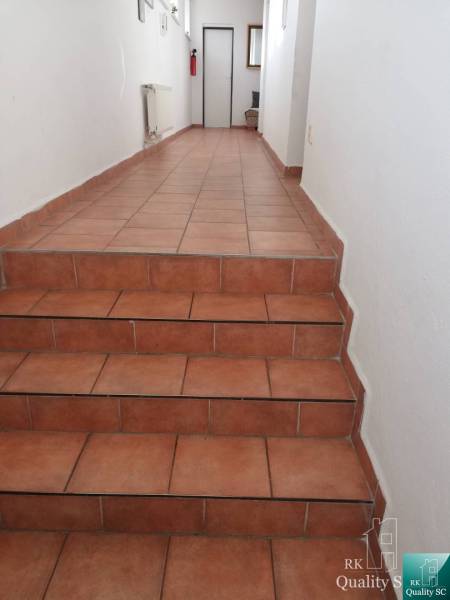 A corridor in a building with white walls and terracotta flooring, leading to white doors.