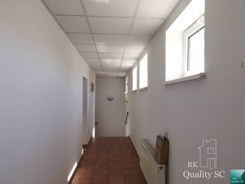 A corridor in a building with white walls, windows, and ceramic flooring.
