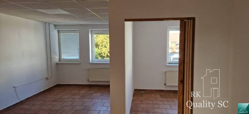 Interior of a building with white walls, brown tiles, and three windows with a view.