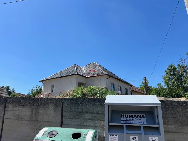 A family house in Sasinkovo on Sasinkovo Street behind a concrete fence with a blue sky.