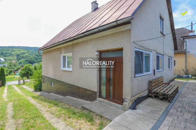 A family house in Dolná Mariková with a grassy yard and a paved access road, surrounded by nature.