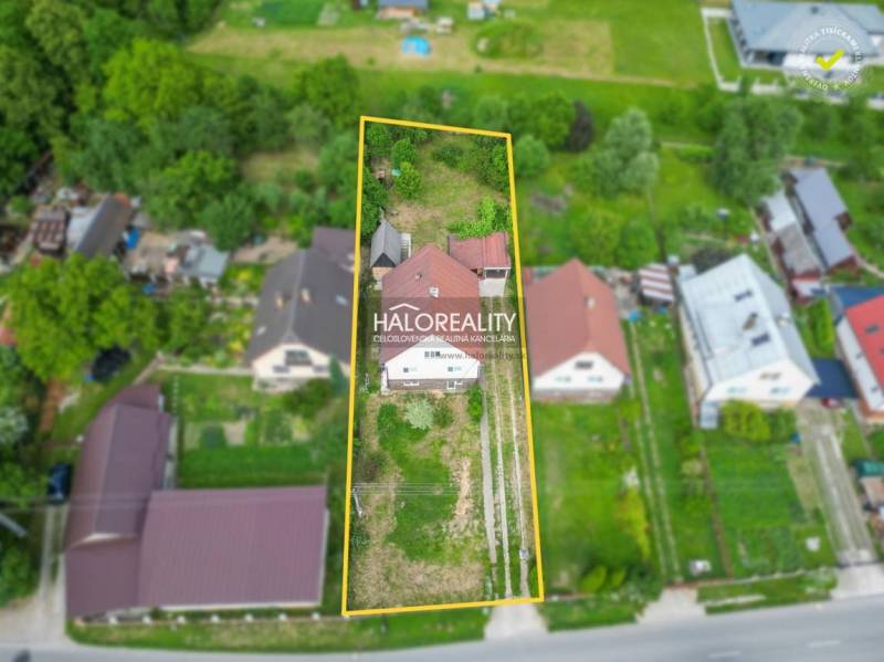 A family house in Dolná Mariková surrounded by greenery and neighboring houses near the road.