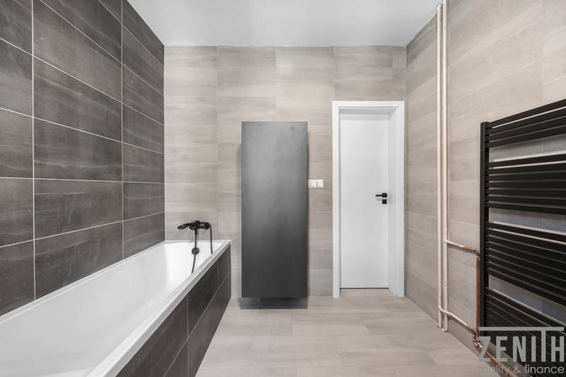 A bathroom with a bathtub, gray tiles, and black accessories in a 3-room apartment.